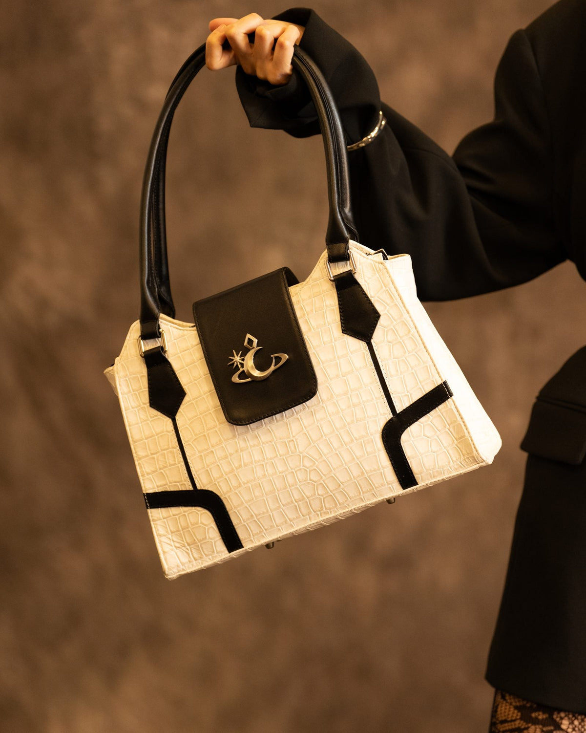 Bolso Halo de Luna Vesper, Sostenido en alto por el asa; de la modelo solo se ve el brazo y la manga. Bolso entero, aislado y